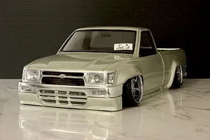 Front three-quarter view of a silver Toyota Hilux RC drift truck body shell on a glossy marble surface.