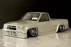 Custom painted silver RC pickup truck body shell with chrome wheels on a marble surface.
