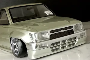 Close-up front angle of the painted silver Toyota Hilux RN80 RC body shell with custom wheels and a lowered stance.