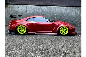 Side profile of a red Nissan GT-R RC drift car body with bright yellow wheels and a large rear wing on asphalt.