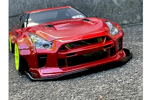 Low angle front view of a red RC drift car body featuring a wide body kit and bright fluorescent yellow wheels parked on asphalt.