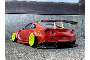 Rear three-quarter view of a red RC drift car with bright yellow wheels and a large rear spoiler parked on asphalt outdoors.
