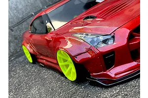 Close-up angled view of a red RC drift car body with wide fender flares and bright yellow wheels parked on asphalt.