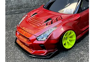 Close-up of a metallic red RC car body shell with bright green wheels on asphalt background.