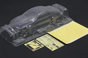 Unpainted clear polycarbonate RC car body shell with mask sheet and decal sheets on a dark surface.
