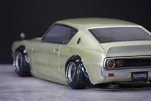 Rear-three-quarter studio view of a gold Pandora RC KPGC110 Skyline 2000GT-R drift car body shell with fender flares.