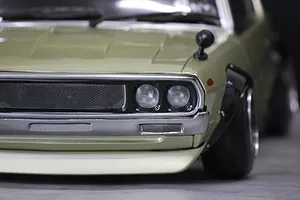 Close-up of the front left corner of a light green KPGC110 Skyline RC car body shell, showing grille, dual headlights, bumper, and fender flare.