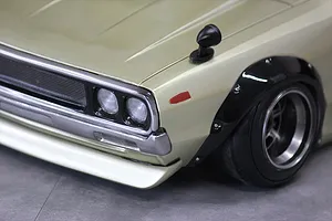 Close-up of the front left corner of a gold RC body shell showing headlights, grille, fender flare, and wing mirror.