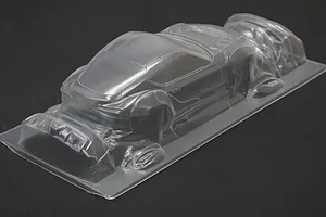Unpainted clear polycarbonate RC car body shell on a dark surface, showing front and rear sections on a single mold sheet.