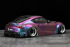 Rear-three-quarter view of a painted Toyota GR Supra RC drift car body shell with a glossy iridescent purple and teal chameleon finish, wide fender flares, and deep-dish wheels.