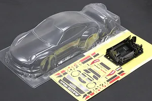 Unpainted clear polycarbonate RC body shell of a Porsche 997 with wide fenders, accompanied by decal sheets and black plastic parts on a dark surface.