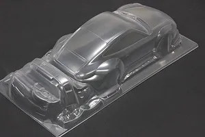 An unpainted, clear polycarbonate RC car body shell of a sports car shown from a high-angle view on a dark background.