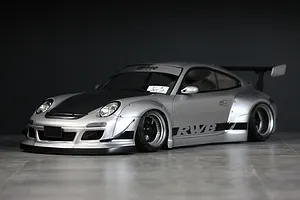 Silver RWB 997 RC drift car body shell mounted on a chassis with wide fenders, black hood, and RWB side graphics against a dark background.