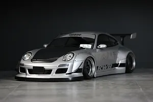 Silver Pandora RC RWB 997 Type drift body shell mounted on an RC chassis with wide fenders, black bonnet, and wing against a dark backdrop.