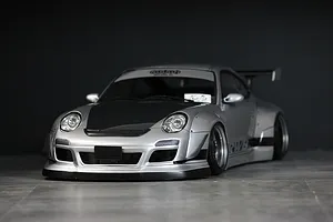 Silver RWB 997 RC drift car body shell with black hood, wide fenders, and rear wing on a dark background.