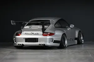 Rear three-quarter view of a silver RWB 997 RC body shell with a large rear wing, quad exhaust tips, and Abu Dhabi branding.