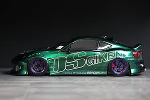 Side view of a metallic green RC drift car body shell mounted on a chassis with purple and black wheels against a dark background.