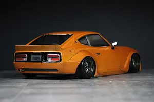 Rear three-quarter view of an orange S30 Fairlady Z RC drift car body shell with fender flares and custom wheels on a dark studio backdrop.