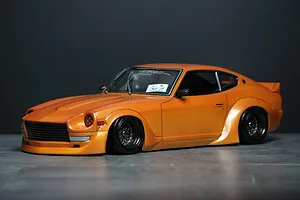 Orange RC drift car body modeled after a Datsun Fairlady Z S30 with wide body kit and mesh wheels on a dark studio backdrop.