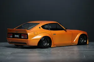 Rear-three-quarter view of an orange S30 Fairlady Z RC car body shell with wide fender flares and deep dish wheels.