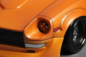 Close-up of the front corner of an orange RC car body shell, showing the headlight, grille, fender flare, and wheel.