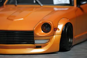 Close-up of the front quarter of an orange RC body shell featuring a detailed headlight, grille, and wide fender flare.