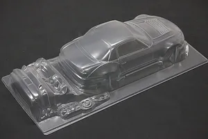 Unpainted clear polycarbonate RC car body shell with additional molded parts on a dark background.