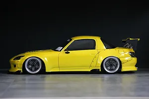 Side profile view of a yellow Honda S2000 RC drift car body shell with a hardtop, large rear wing, and widebody fenders against a dark background.