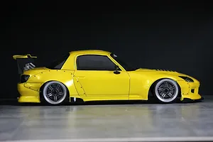 Side profile view of a yellow radio-controlled Honda S2000 drift car body shell with a rear wing and black wheels.