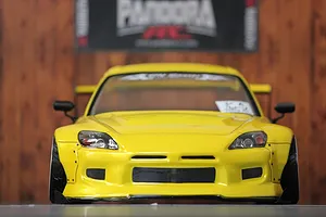 Front view of a yellow radio-controlled Honda S2000 drift car body shell parked indoors against a wooden wall.