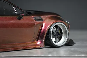 Close-up of a metallic bronze RC drift car body showing the front fender, wheel, and side mirror against a neutral background.