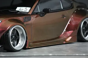 Close up side profile of a custom RC drift car body with brown metallic paint, wide fenders, and deep dish wheels.