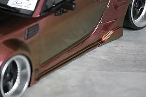 Close-up of the side profile and skirt of a metallic maroon RC drift car body with widebody fender flares and deep-dish wheels.