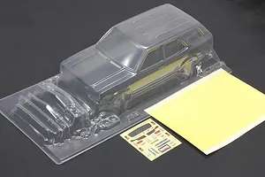 Unpainted clear polycarbonate RC car body shell with separate parts, decal sheet, and window mask on a dark background.