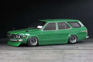 Green RC drift car body styled as a classic station wagon with custom wheels, parked on a grey studio floor against a dark background.