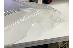 Unpainted clear polycarbonate RC car body shell resting on a white workbench surface.