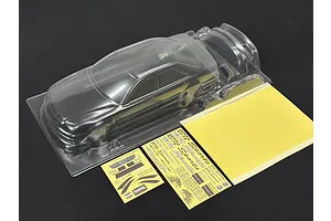 Unpainted clear polycarbonate RC car body shell with window masks and decal sheets on a dark surface.