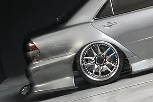 Close-up of the rear quarter section of a silver RC drift car body showing the wheel, tire, taillight, and exhaust.