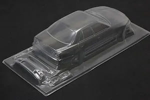 Unpainted clear polycarbonate RC drift car body shell with separate parts molded on a sheet against a dark background.