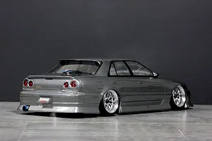 Rear three-quarter view of a grey Pandora RC ER34 Skyline 4-door drift RC car body shell with custom wheels and exhaust tip on a studio floor.