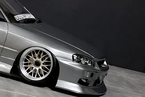 Close-up front quarter view of a silver RC drift car body shell showing the front wheel, bumper, and headlights against a dark background.