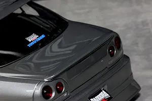 Close-up rear angle of a grey RC car body shell, showing trunk lid, rear lights, spoiler, and branded decals.
