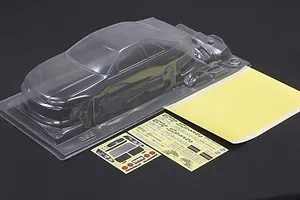 Clear unpainted polycarbonate 1/10 scale RC car body shell with window masks and decal sheets on a dark surface.