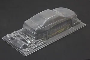 Unpainted clear polycarbonate 1/10 scale RC car body shell with separate parts tray on a dark surface.