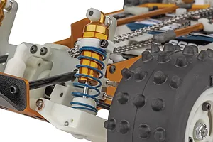 Close-up of the RC buggy suspension showing a gold anodized shock absorber with a blue spring, off-road tire, and drive chain.