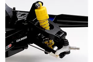 Close-up of front suspension on a Tamiya RC buggy showing a yellow C.V.A. shock absorber, black plastic arms, and metal steering linkage.