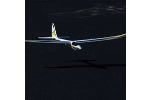 E-Flite UMX Conscendo RC glider in flight, showing its white, yellow, and black livery above an asphalt surface.