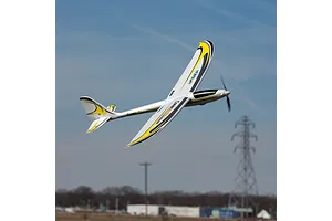 E-Flite UMX Conscendo RC glider in flight against a blue sky with distant power pylons and buildings.