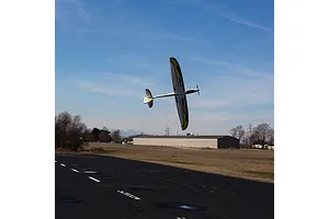 An E-Flite UMX Conscendo RC glider banking in flight above an asphalt airstrip against a blue sky.