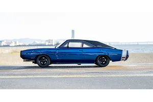 Side profile view of the Kyosho Fazer MK2 1970 Dodge Charger RC car in blue, parked outdoors near the coast with a distant city skyline.